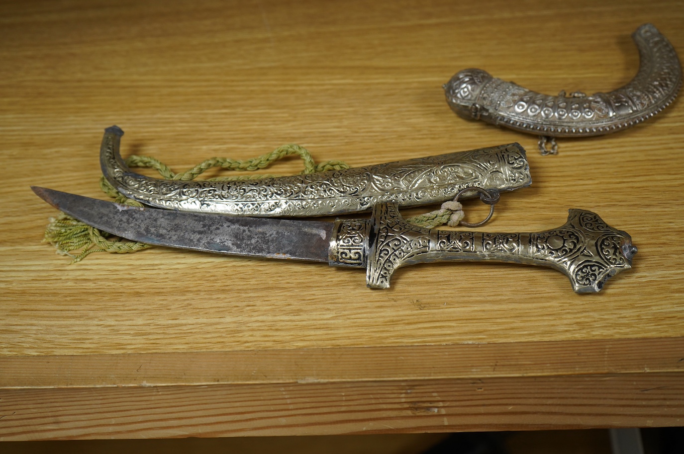 An Omani silver spice box in the form of a curved powder flask, together with a Moroccan dagger Jambiya with nickel hilt and sheath, both 20th century. Condition - fair.